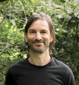 A photo of Luke Kaplan with green leaves in the background