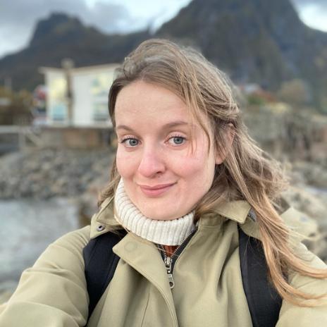 A student with blonde hair smiling by a coastal background