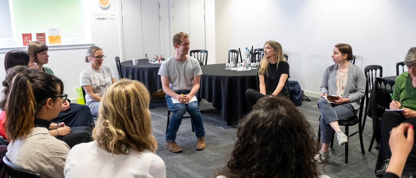 A group of people seated in a circle during a workshop discussion in a bright room