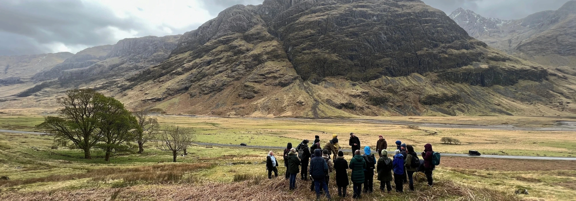 A group of scholars huddling together in the wide expansive landscape of Glencoe, Scotland