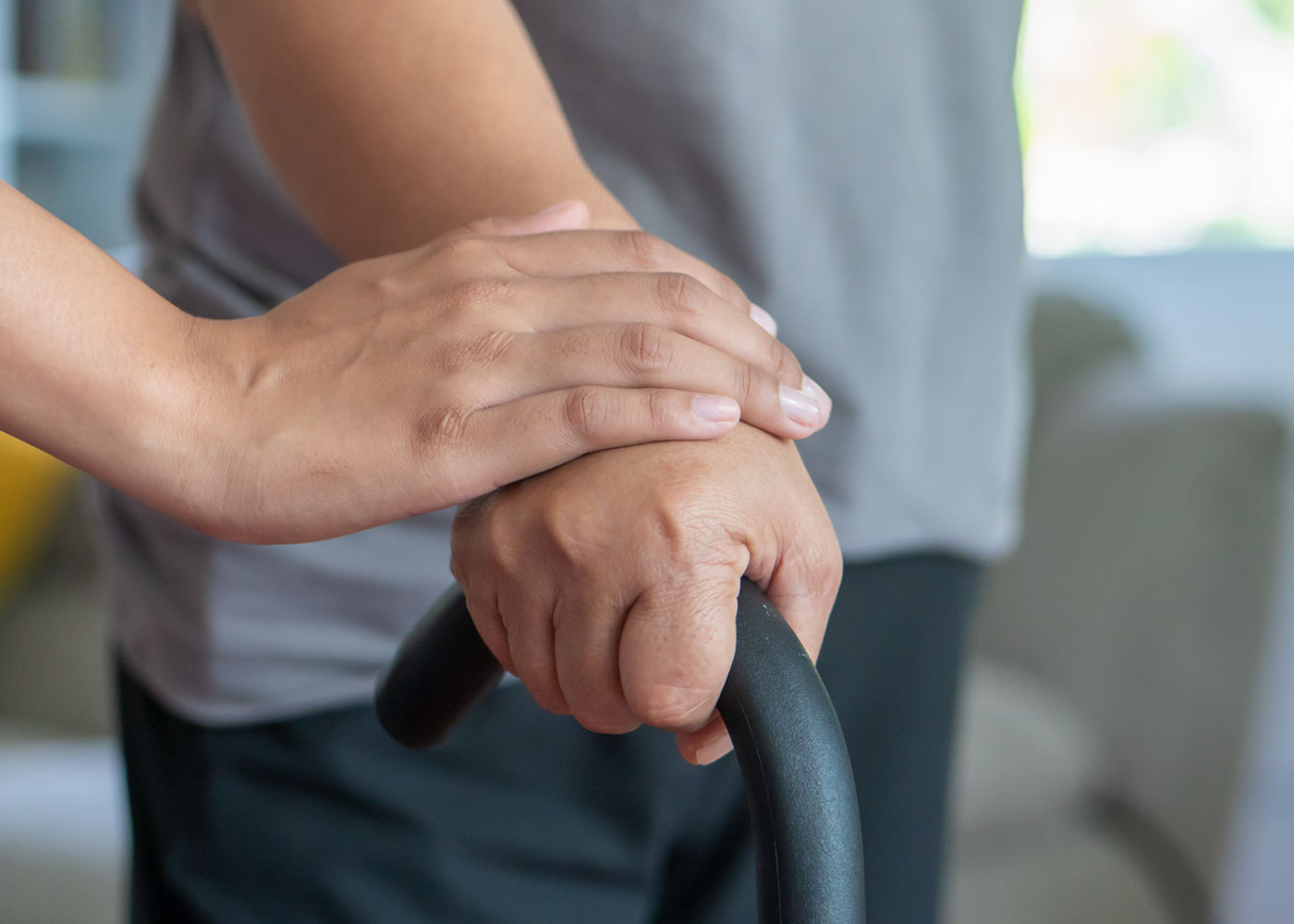 close up of a person holding a walking stick with another person's hand on top of their hand. love and care concept.