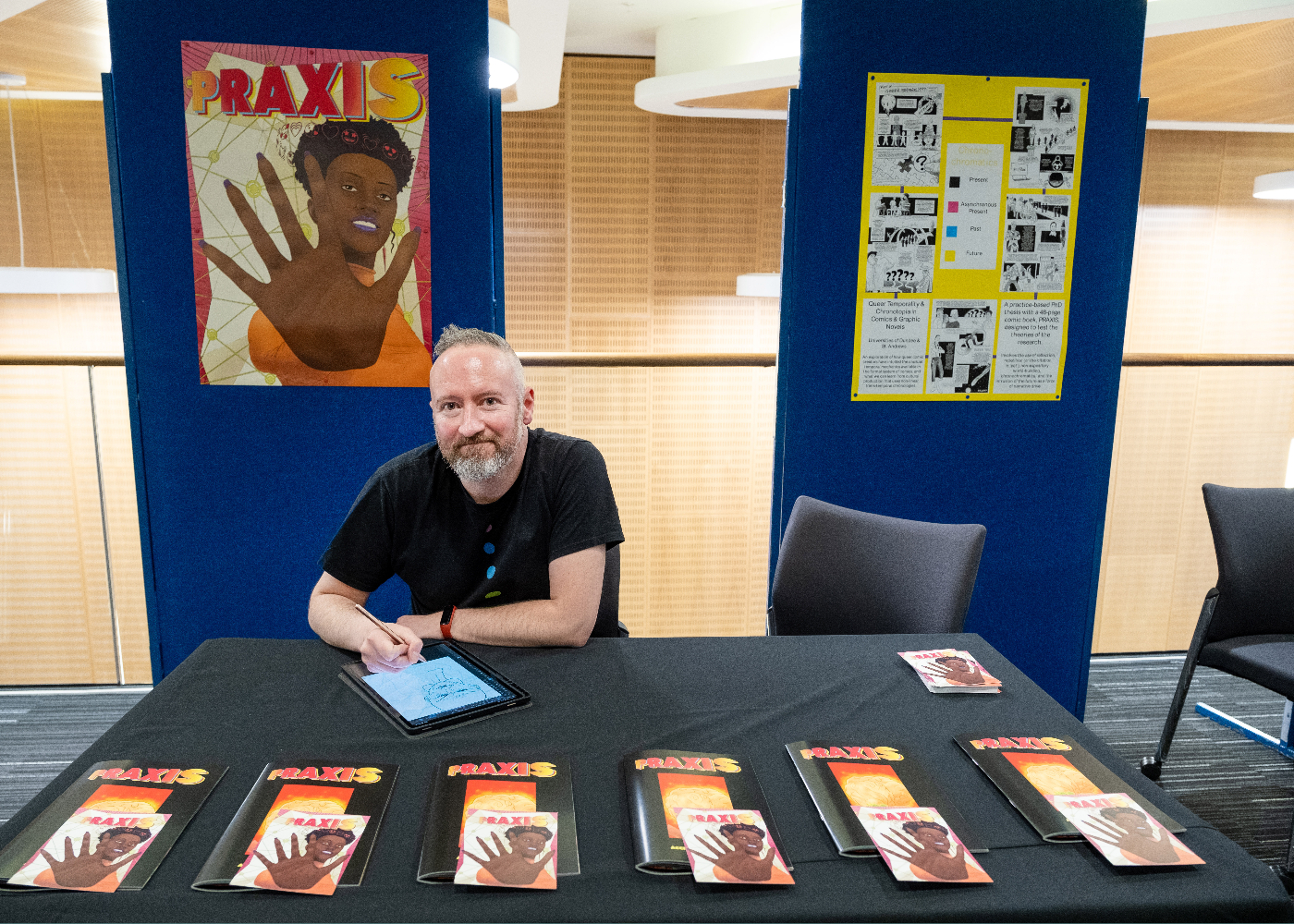 Research Showcase exhibitor, Garry McLaughlin, seated at a table showcasing his exhibition of graphic novels